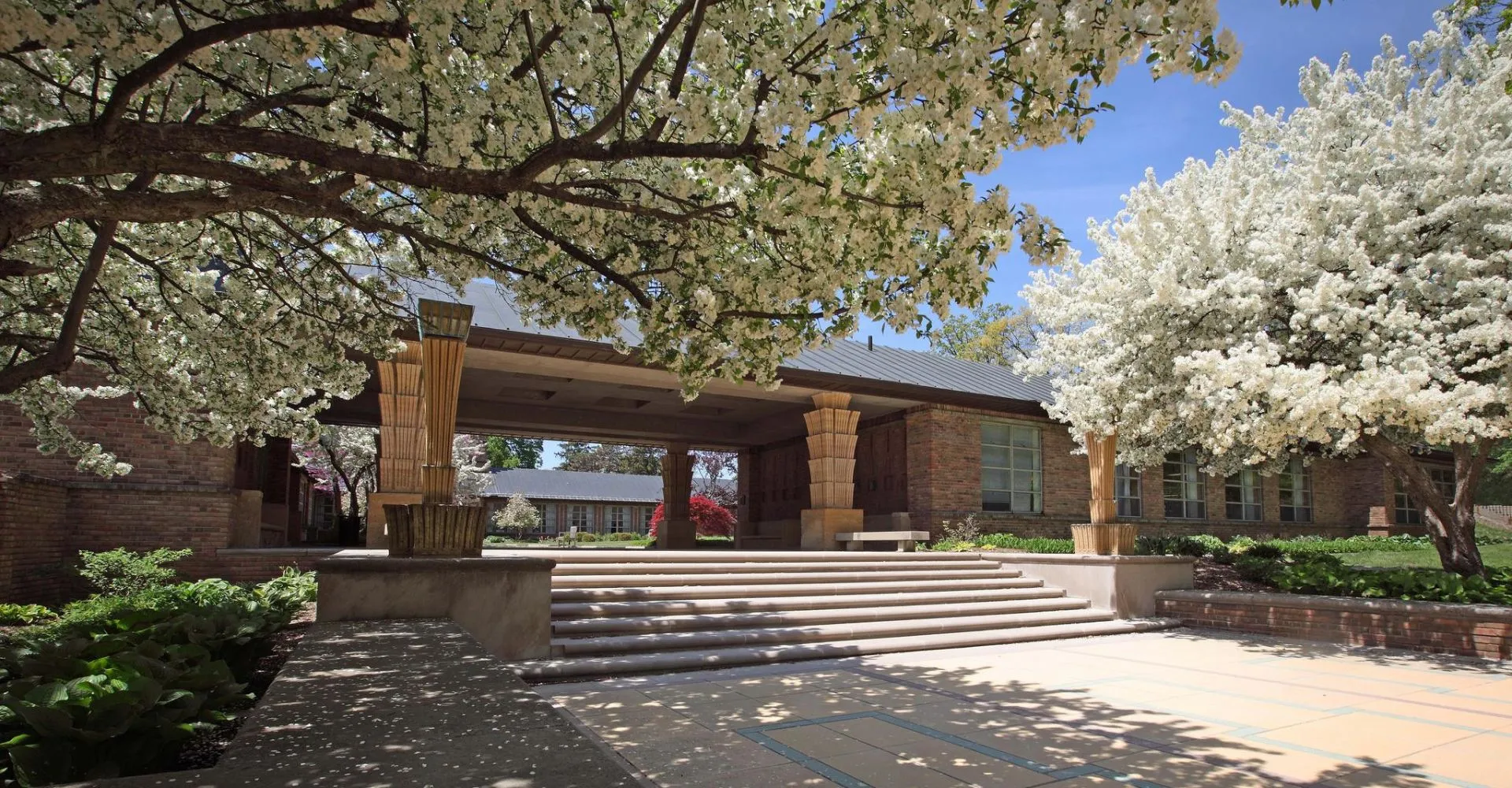 L'edificio in mattoni con ingresso coperto della Cranbrook Schools è circondato da alberi in fiore e da un viale lastricato.