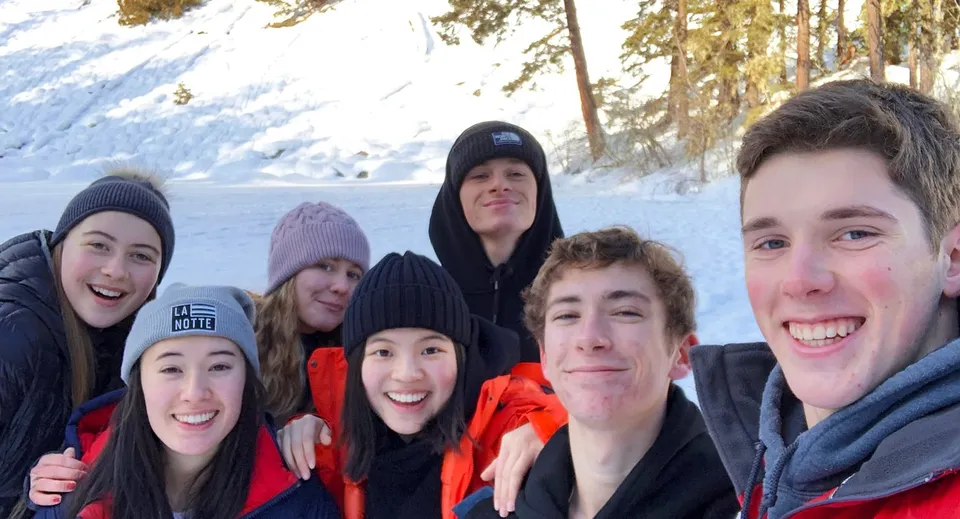 Studenti della Prince of Wales Secondary School sono insieme in un bosco innevato con abbigliamento invernale caldo.