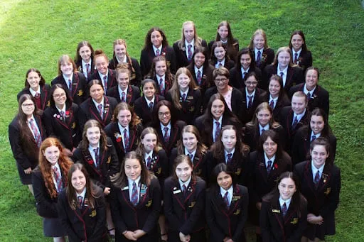 Un gran grupo de alumnas de la Hamilton Girl's High School está de pie en un campo de hierba.