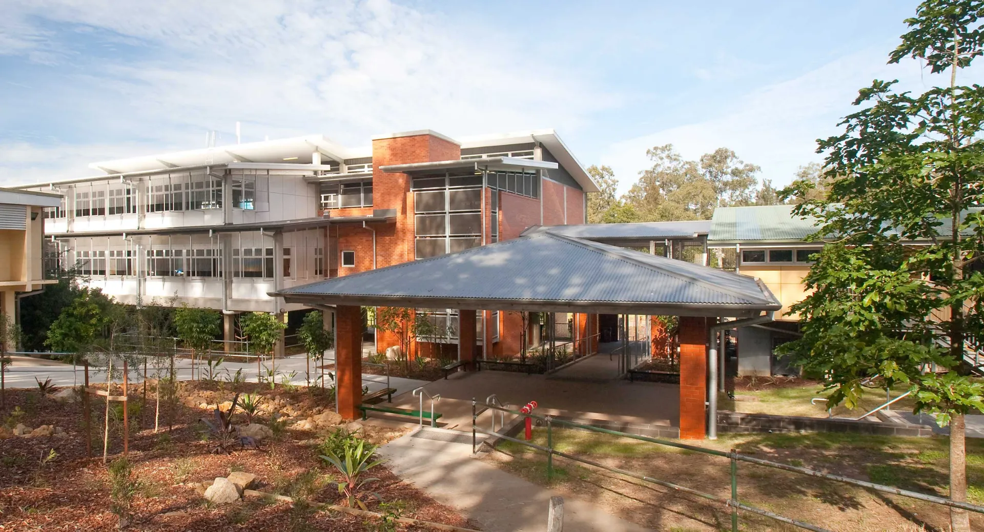 L'edificio moderno a più piani della Kenmore State High School con facciata in vetro ed area esterna coperta circondata da alberi.