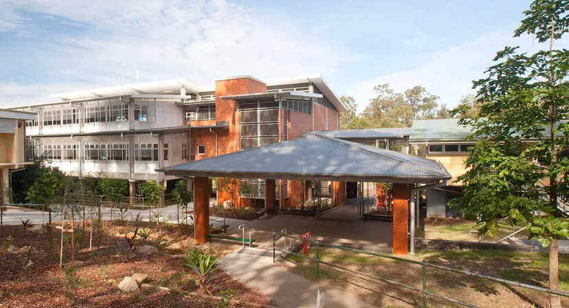 L'edificio moderno a più piani della Kenmore State High School con facciata in vetro ed area esterna coperta circondata da alberi.