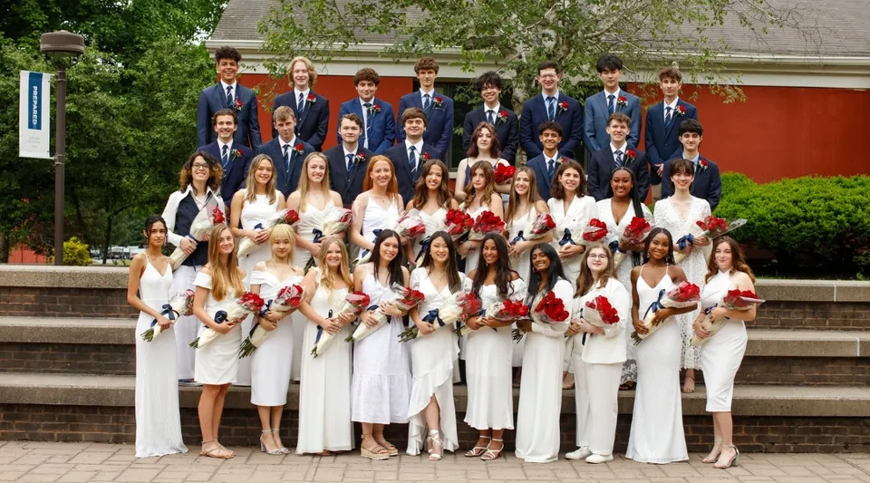 Un grande gruppo di persone in abito formale si trova sulla scalinata davanti a un edificio nel campus della Allendale Columbia School.