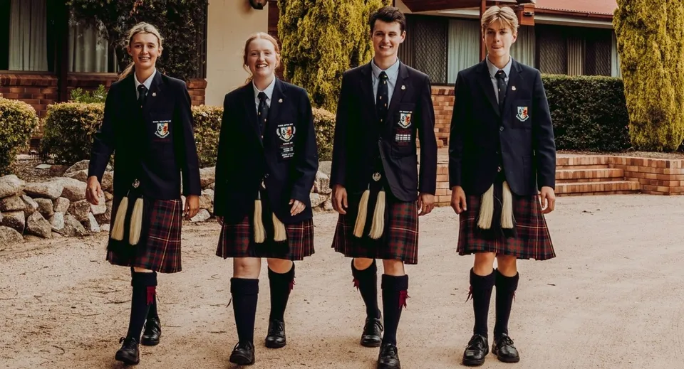 Quattro studenti in divisa scolastica sono in piedi davanti all'edificio in mattoni nel campus del Scots PGC College.