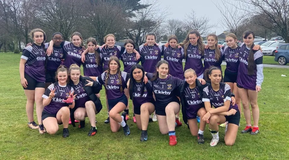Un gruppo di giovani calciatrici posa sul campo sportivo della Colaiste Muire Mathair con maglie viola.