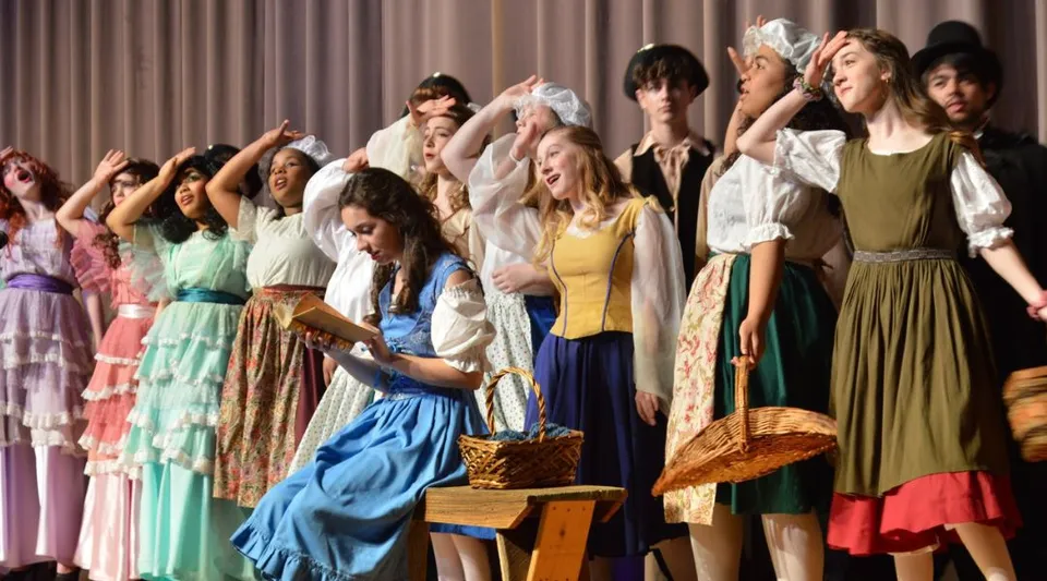 Un gruppo di donne in abiti retrò colorati posa sul palco della Atlantic Shores Christian School.