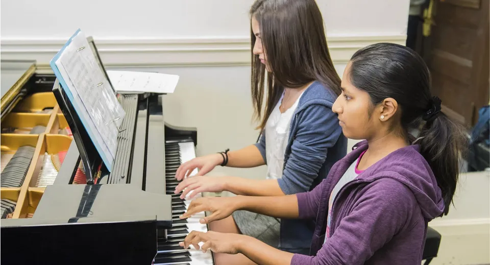 Due studentesse suonano il pianoforte insieme nel campus della Canada Star Secondary School.
