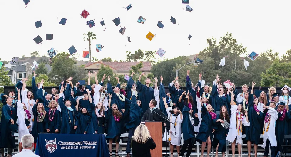 I diplomati della Capistrano Valley Christian School festeggiano il loro diploma davanti a palme ed edifici scolastici.