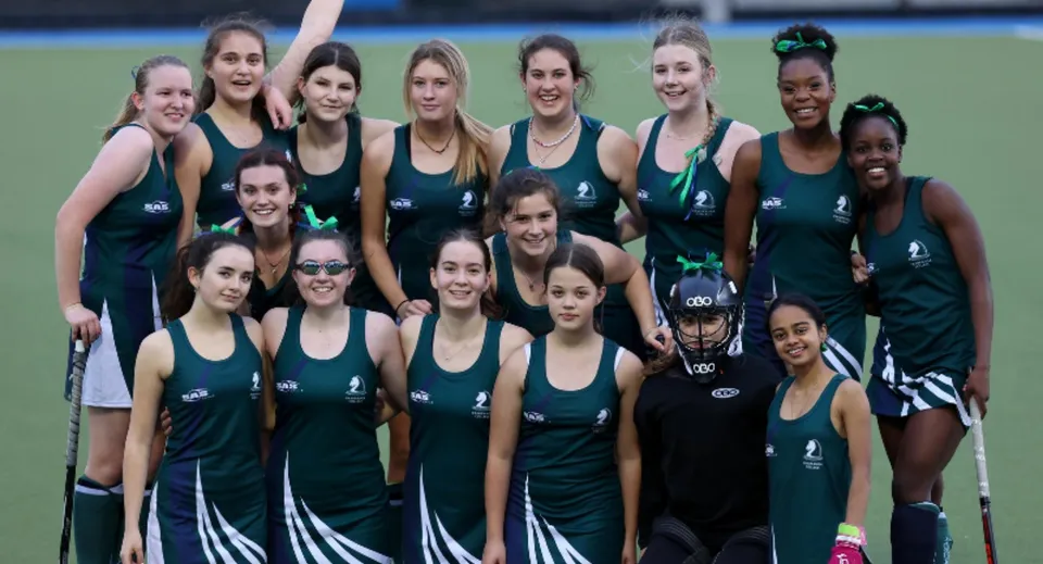 Un gruppo di giovani atlete con maglie uniformi verdi e nere in piedi sul campo sportivo del Pakuranga College.