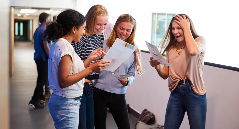 Quattro studentesse del David Game College guardano sorridenti dei documenti nel corridoio della scuola.