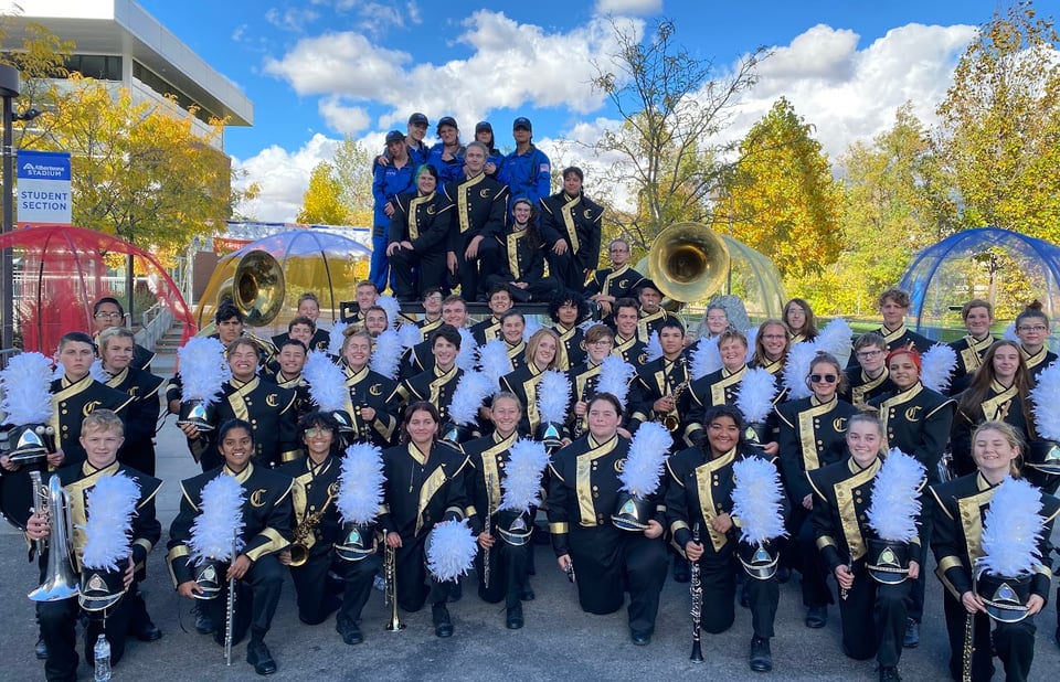 Gruppenbild von der Marching Band der Schule draußen umgeben von Bäumen