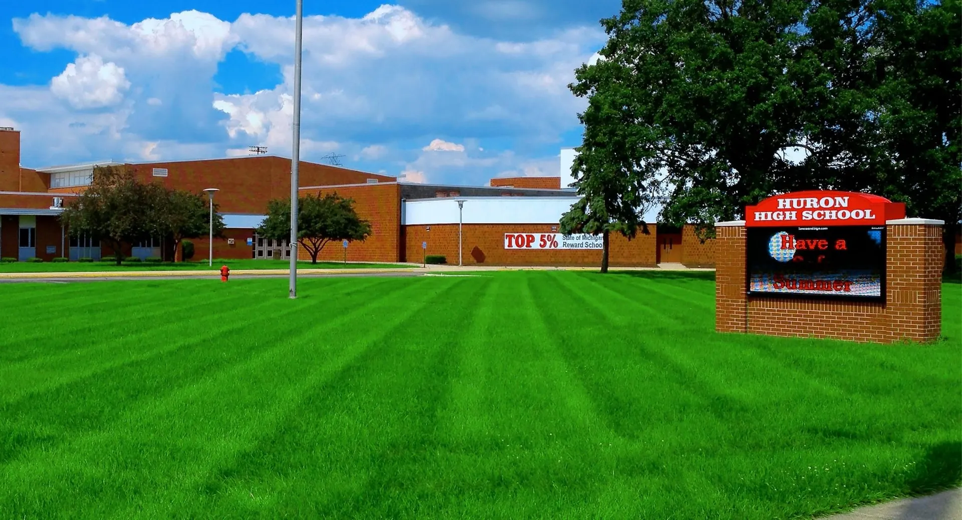 L'edificio della Huron High School si trova dietro un prato verde ben curato sotto un cielo blu con nuvole bianche.