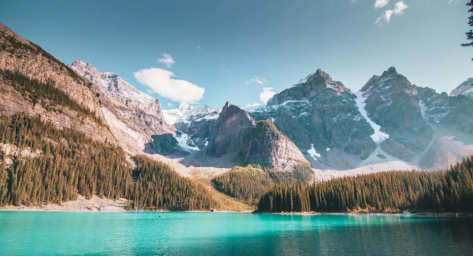 Un lago alpino con montagne innevate e una foresta verde in primo piano vicino alla North Delta Secondary School.