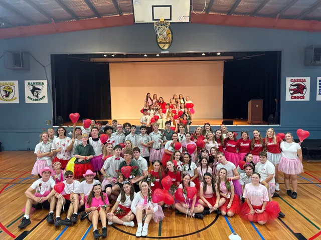 Alumnos vestidos de rojo y rosa con globos de corazón posando en el pabellón del colegio