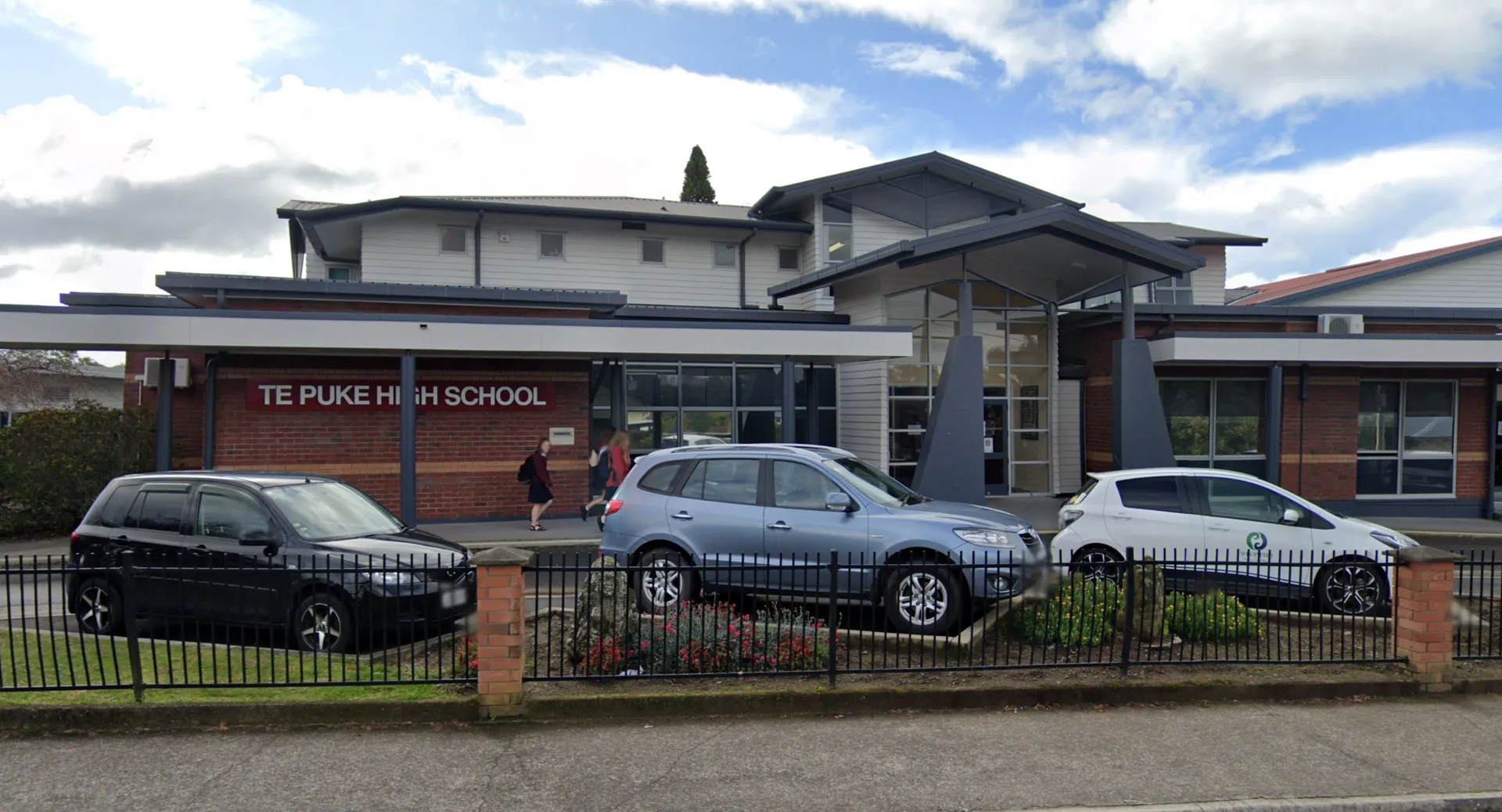 L'edificio scolastico moderno della Te Puke High School con un cartello è circondato da auto parcheggiate.