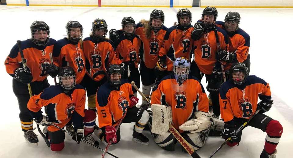 Un gruppo di giovani giocatori di hockey in maglia arancione e nera sulla pista da ghiaccio della Bayridge Secondary School.