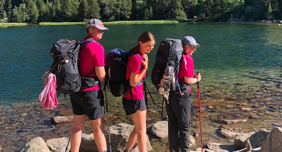 Un gruppo di studenti e studentesse della Hereford Cathedral School si trova sulla riva di un lago turchese in mezzo a una foresta di conifere.