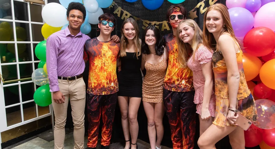 Un gruppo di studenti della Northfield Mount Hermon School posa insieme davanti a uno sfondo decorato a festa.