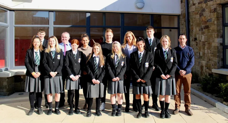 Un gruppo di studenti del Newbridge College in abito da diploma sta davanti a un edificio.