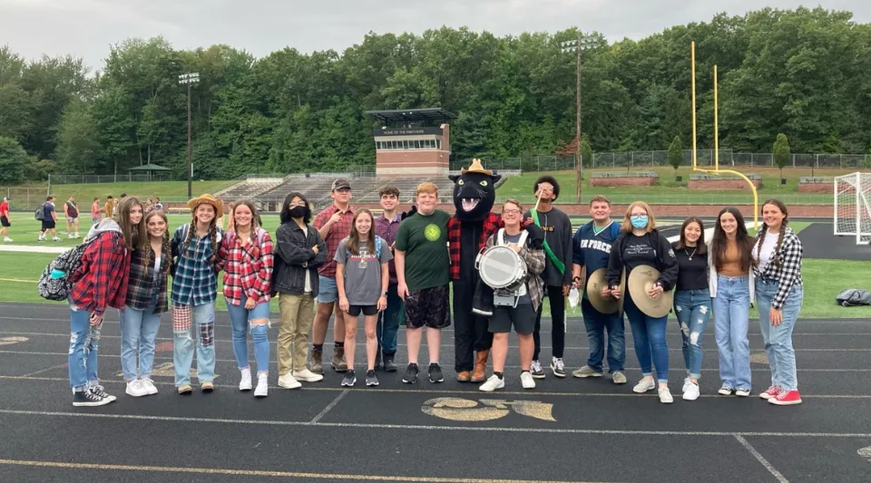 Un gruppo di studenti si trova sul campo sportivo della Comstock Park High School accanto ad attrezzature sportive e alberi.