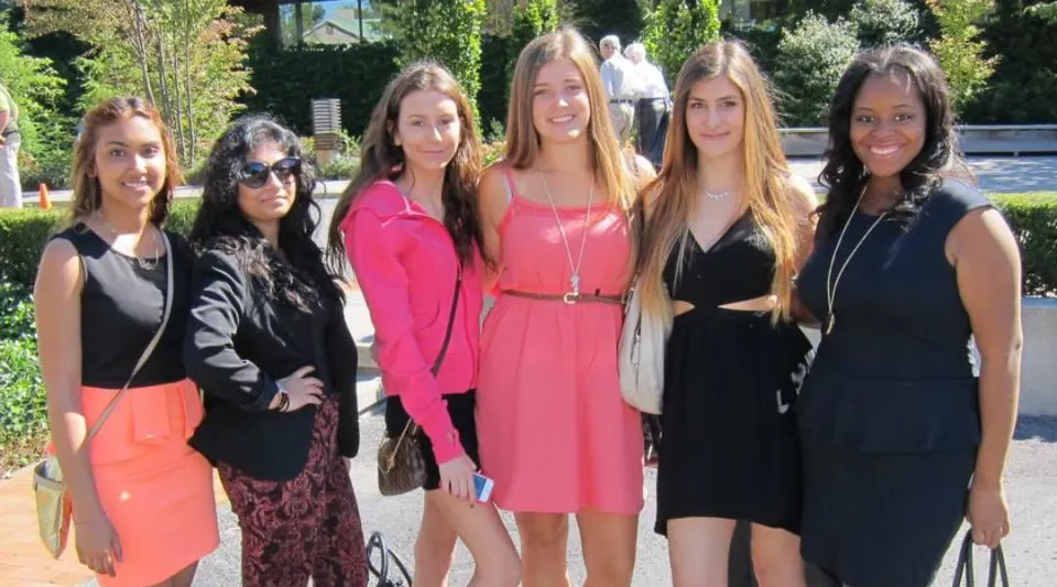 Un gruppo di sei studentesse si trova all'aperto nel campus della Pine Ridge Secondary School davanti a un edificio e a un ambiente verde.
