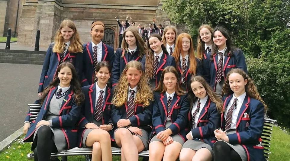 Un gruppo di giovani studentesse in divisa scolastica siede su una panchina davanti a un edificio storico della Royal School Armagh.
