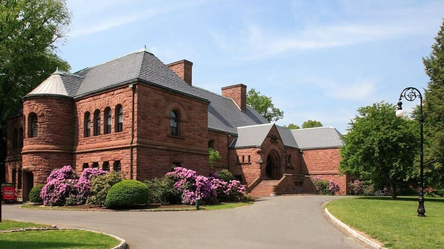 Historisches Schulgebäude aus rotem Sandstein mit Auffahrt und blühenden Rhododendren