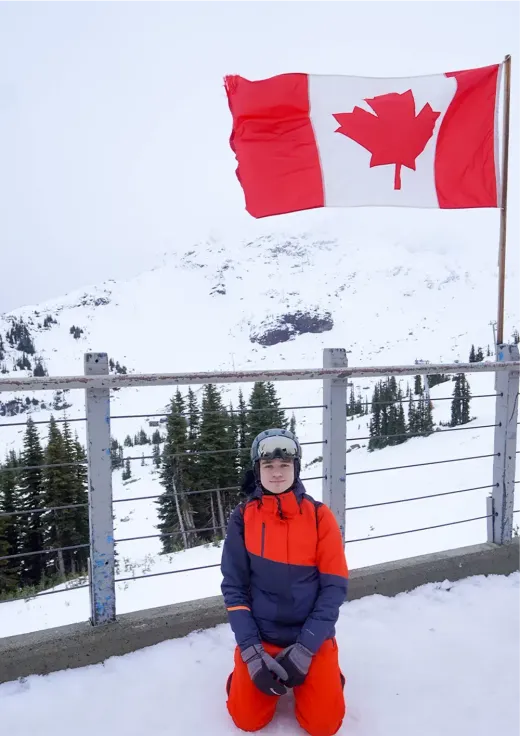 Stefan im Skianzug kniet im Schnee unter einer kanadischen Flagge in den Bergen