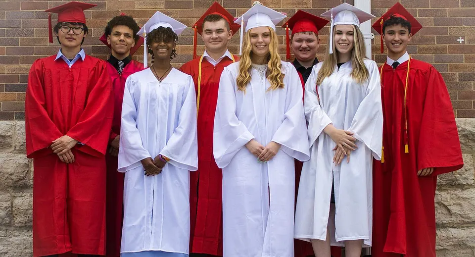 Un gruppo di diplomati della Dominion Academy of Dayton è in piedi davanti a un muro di mattoni e festeggia il proprio diploma.