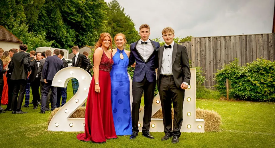 Un gruppo di studenti del Stratford College in abiti formali si trova davanti alla scultura del numero 2 su un prato con alberi.