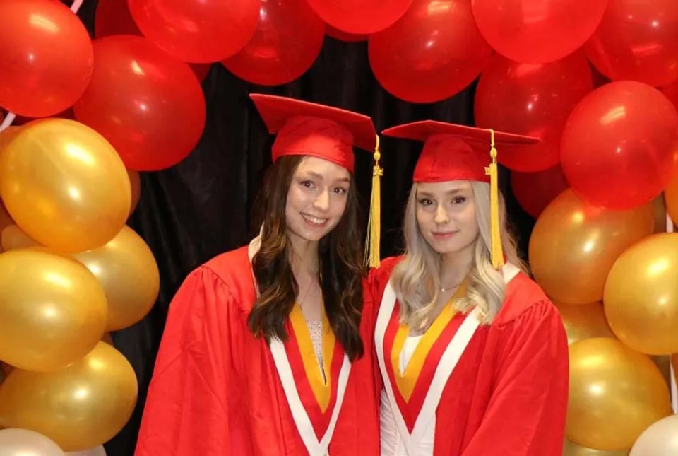 Due diplomande della Hammarskjold High School posano nei loro abiti da cerimonia davanti a palloncini rossi e dorati.