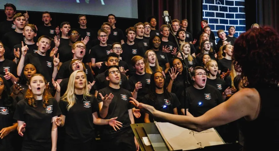 Un grande gruppo di studenti della Trinity Catholic High School sta su un palco davanti a una parete in mattoni.