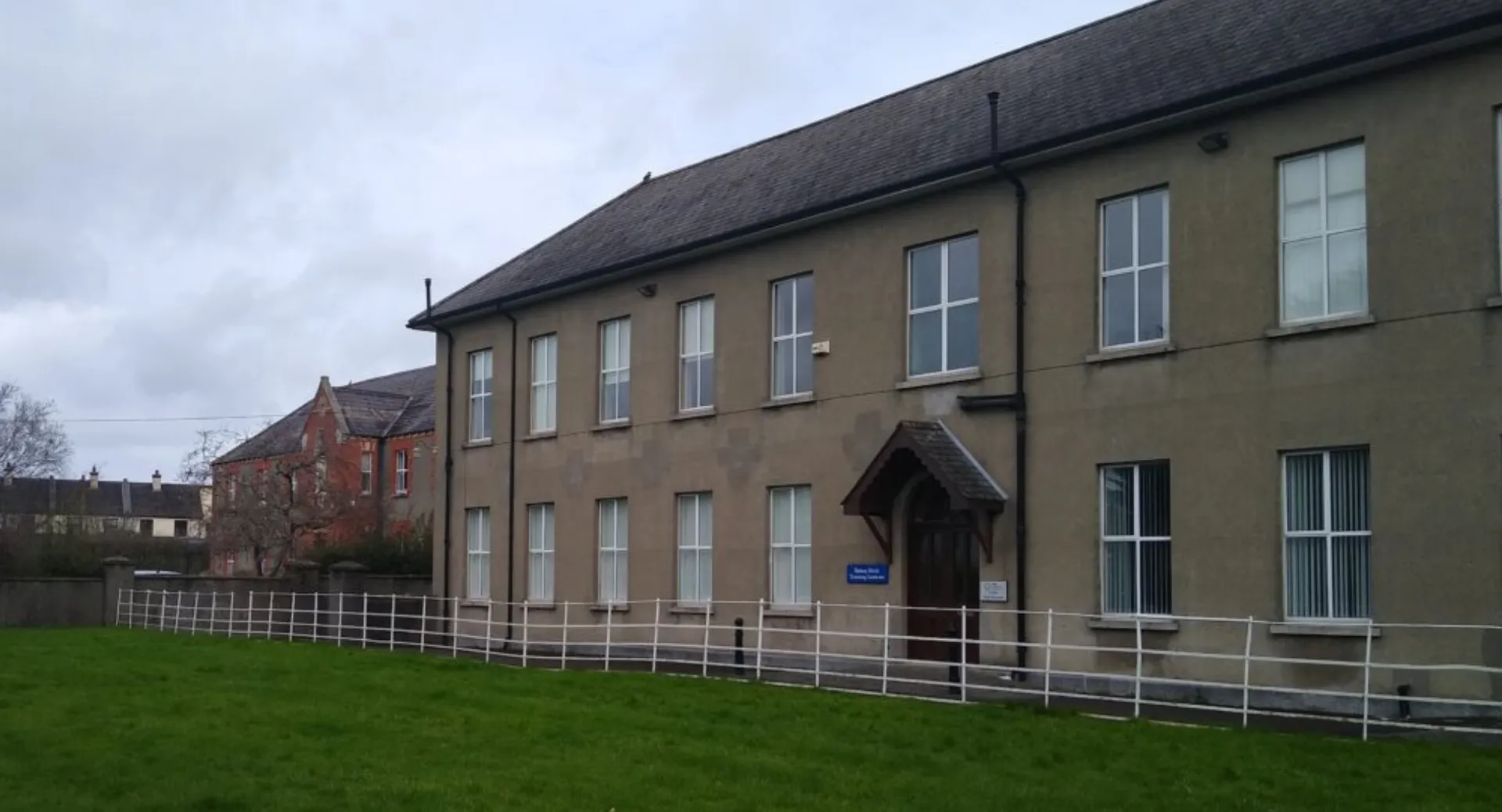 L'edificio in mattoni a più piani della Kilkenny City Vocational School con tetto a spiovente si trova davanti a un cielo nuvoloso.