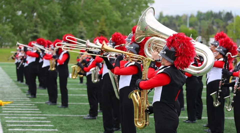 La Marching Band della Our Lady of the Rockies High School si esibisce su un prato con un bosco sullo sfondo.