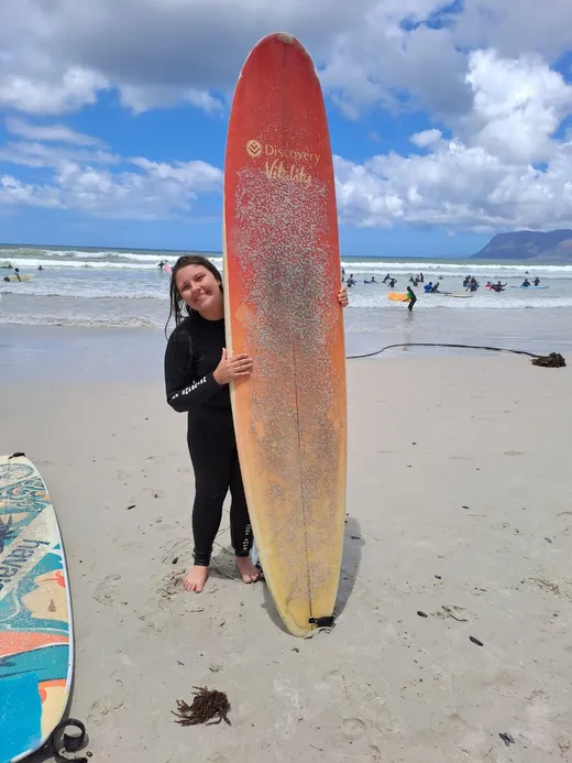 Studentessa in muta tiene una tavola da surf sulla spiaggia durante un corso in Sudafrica