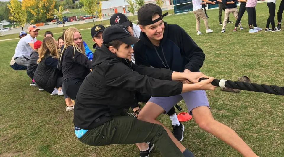 Un gruppo di studenti e studentesse della National Sport School gioca su un campo sportivo con edifici e alberi sullo sfondo.