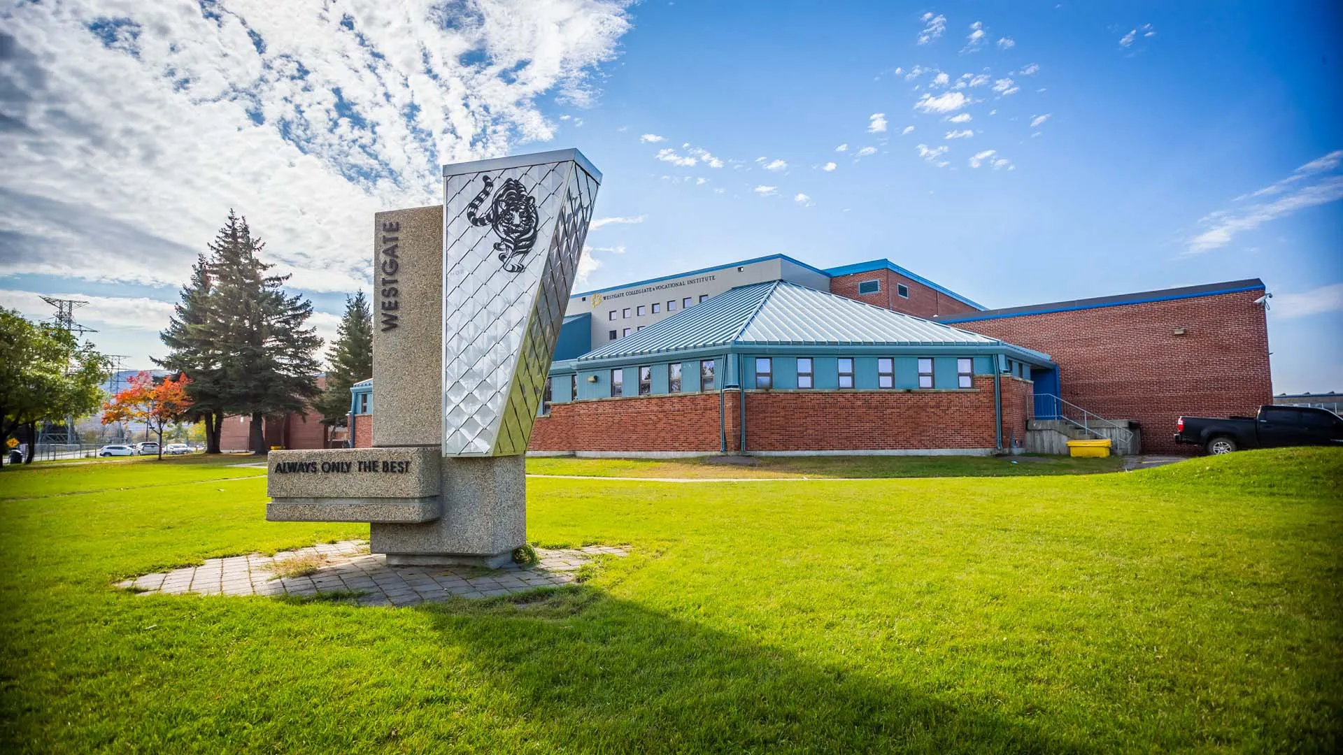 Il Westgate Collegiate & Vocational Institute mostra un monumento decorativo sul prato davanti a un edificio in mattoni con un'alta torre.