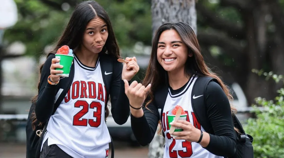 Due studentesse della Hawaiian Mission Academy in maglia sportiva tengono in mano bicchieri di granita all'aperto.