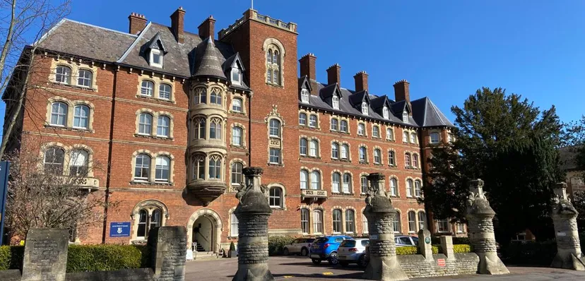 L'edificio principale storico della Malvern St. James Girls' School con una torre e circondato da alberi sotto un cielo limpido.