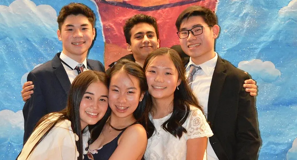 Un gruppo di studenti della Point Grey Secondary School posa davanti a uno sfondo colorato con nuvole.
