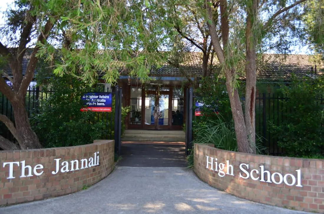 La entrada de la Jannali High School con muros de ladrillo, árboles y puertas de cristal.