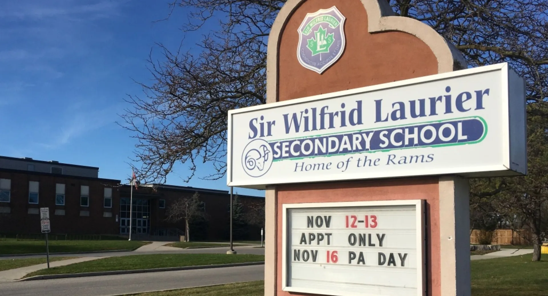 L'insegna della Sir Wilfrid Laurier Secondary School mostra informazioni sulle date con uno sfondo di alberi e cielo blu.