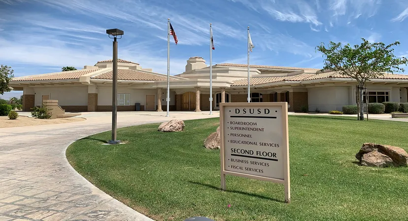 L'edificio amministrativo delle Desert Sands Schools con diverse bandiere e un prato ben curato in primo piano.