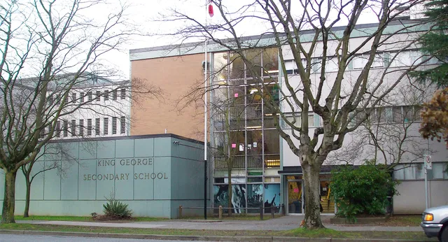 El edificio de ladrillo de la King George Secondary School se ve con árboles desnudos en primer plano.