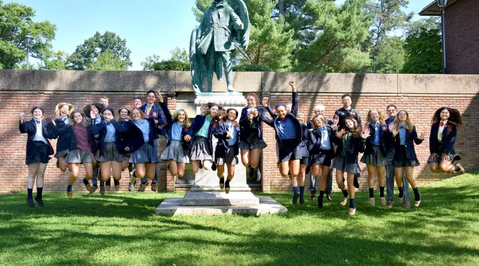 Un gruppo di studenti e studentesse della The Linsly School davanti a un monumento nel campus con alberi ed edifici sullo sfondo.