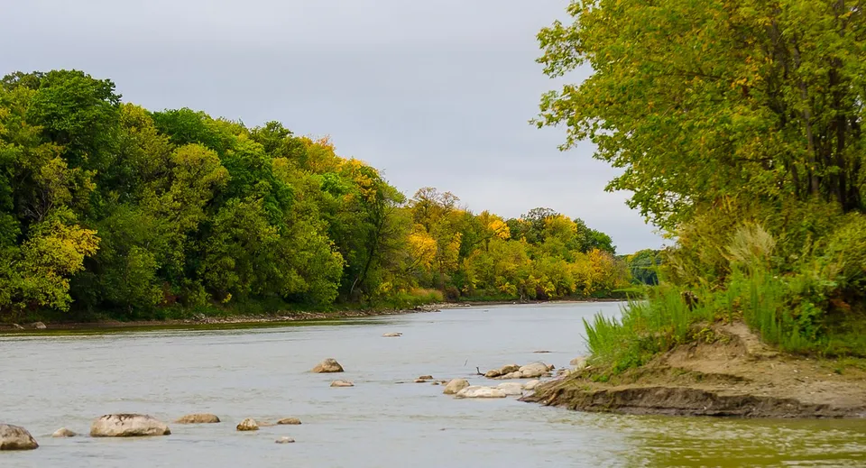 Un fiume tranquillo scorre attraverso un paesaggio autunnale con alberi colorati vicino al Miles Macdonell Collegiate.