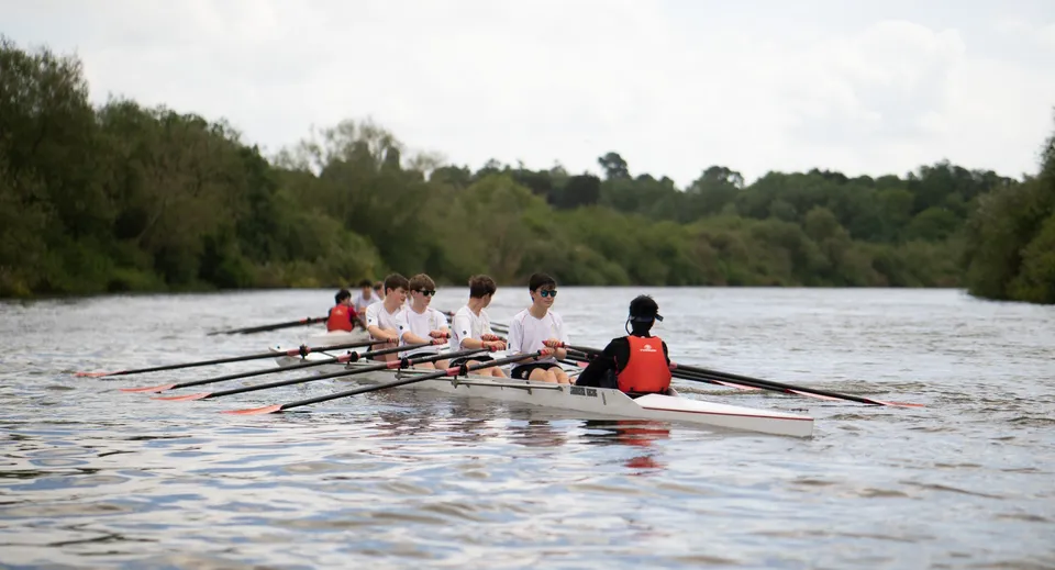Studenti del Cheltenham College remano insieme su una barca lungo un fiume.