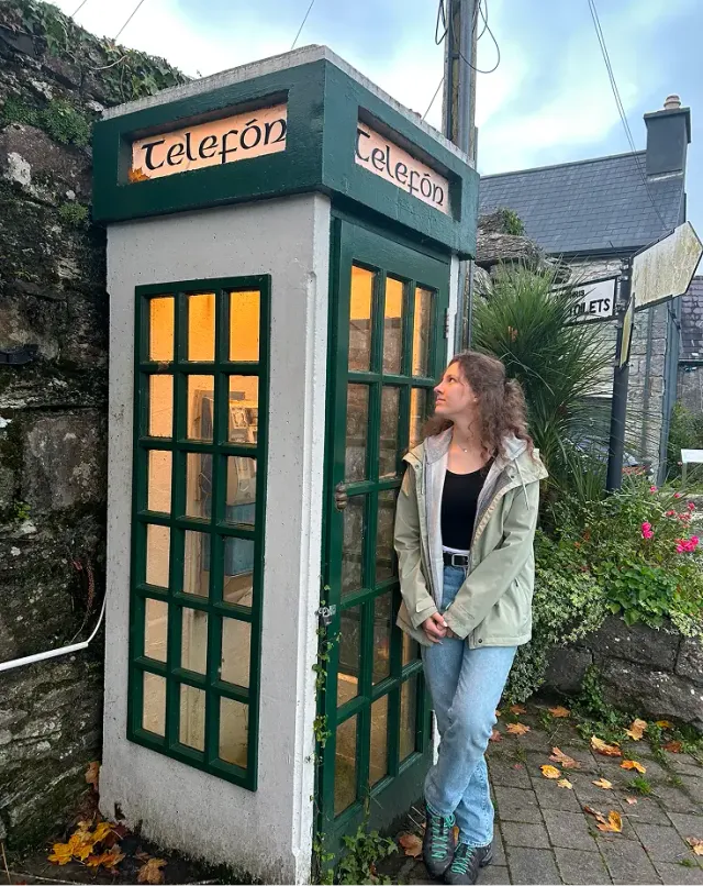 Studentessa accanto a una cabina telefonica verde irlandese con la scritta Telefón