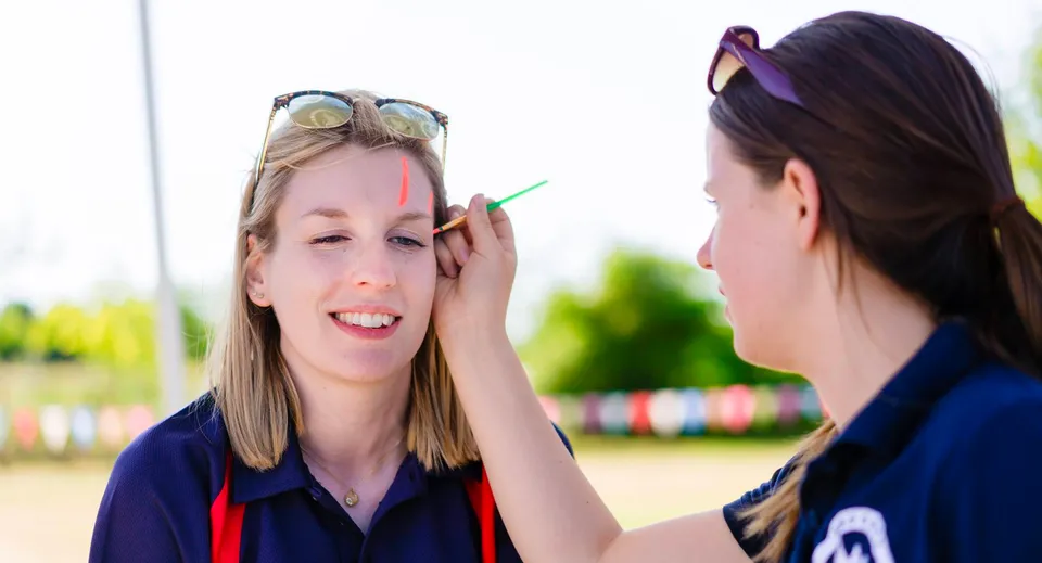 Due studentesse della Brookes UK svolgono un'attività ludica all'aperto con occhiali da sole colorati e decorazioni.