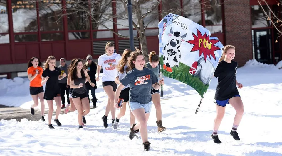 Un gruppo di studentesse della Vermont Academy porta un grande striscione colorato attraverso uno spazio esterno innevato.