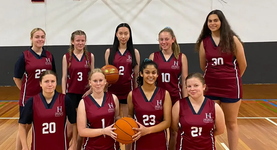 Un gruppo di giovani studentesse in divisa color bordeaux posa con palloni da basket sul campo da basket della The Heights School.